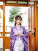 A woman in a purple and white kimono standing in front of a door.