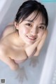 A woman in a bathtub smiling at the camera.