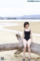 A woman in a black bathing suit sitting on a log on the beach.