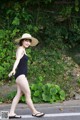 A woman in a black bathing suit and a straw hat crossing the street.