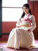 A woman in a white and pink hanbok sitting on the floor.