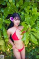 A woman in a red bikini posing in front of a bush.