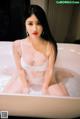 A woman in a white lingerie sitting in a bathtub.