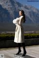 A woman in a white coat standing on a wooden platform.